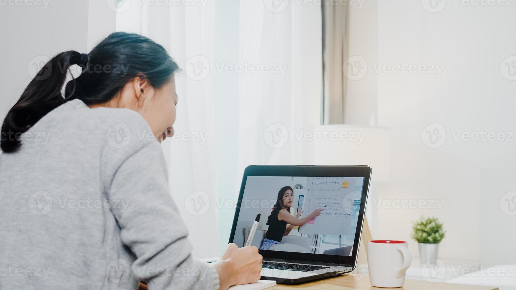 Young Asia teen girl university student using laptop computer distance learn lesson with female teacher remote teaching on internet at home. Social distancing, quarantine for corona virus prevention. photo
