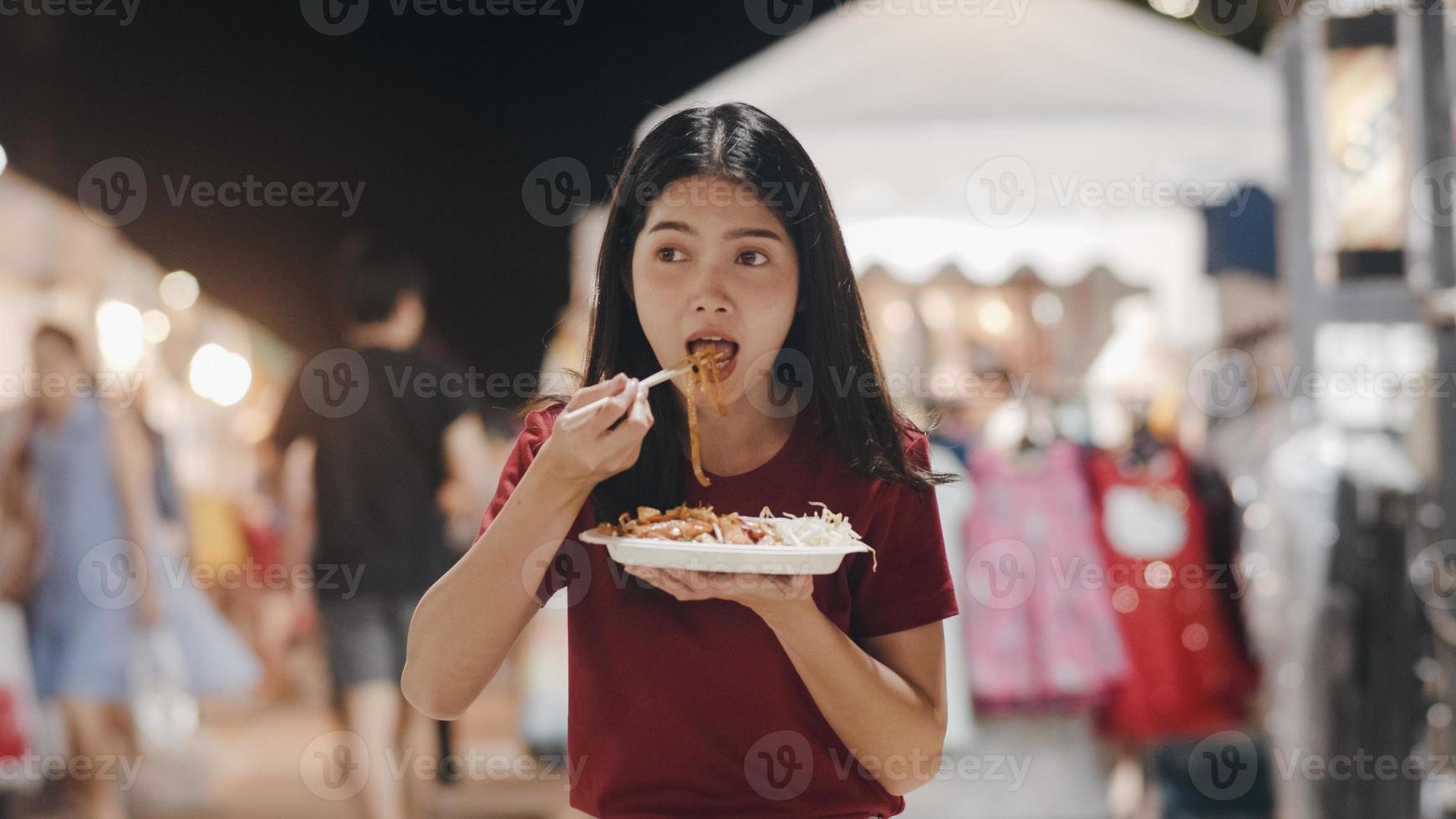 Asian young woman travel in Bangkok, Thailand, beautiful female feeling happy walking and eating Pad Thai at The Khao San Road. Women travel eat street food in Thailand concept. photo