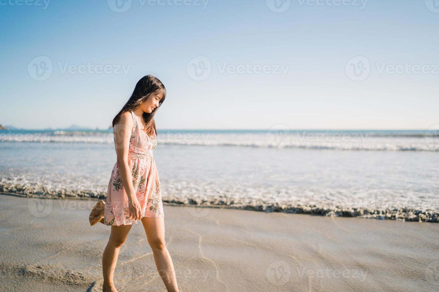 Young Asian woman walking on beach. Beautiful female happy relax walking on beach near sea when sunset in evening. Lifestyle women travel on beach concept. photo