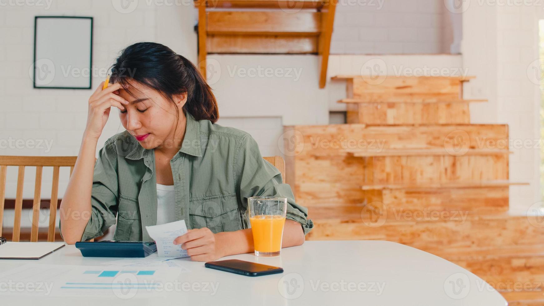 Business Asian women records of income and expenses at home, Young Asia girl worried, serious, stress while using laptop record budget, tax, financial document working in kitchen concept. photo