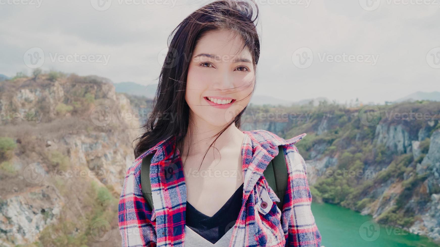 excursionista mujer mochilera asiática que se siente feliz sonriendo a la cámara en la cima de la montaña, la mujer disfruta de sus vacaciones en una aventura de senderismo sintiendo libertad. las mujeres de estilo de vida viajan y se relajan en el concepto de tiempo libre. foto