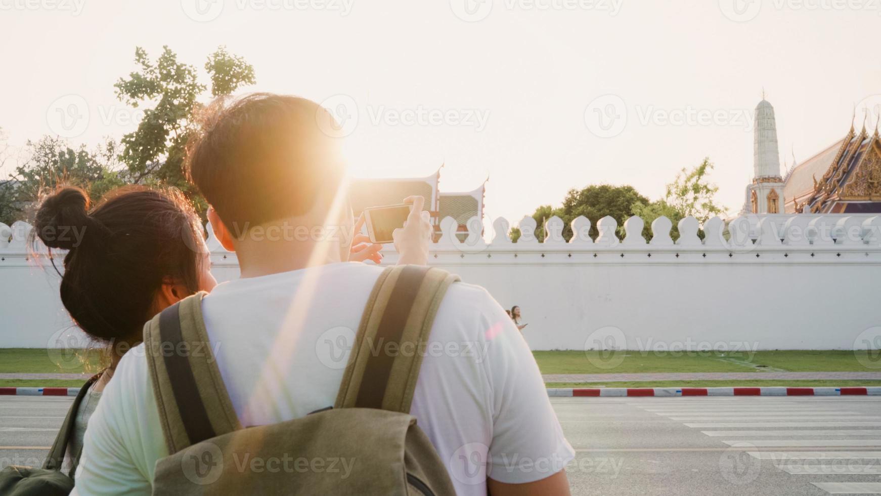 Traveler Asian couple using mobile phone for take a picture while spending holiday trip at Bangkok, Thailand, couple enjoy journey at landmark in sunset. Lifestyle couple travel in city concept. photo