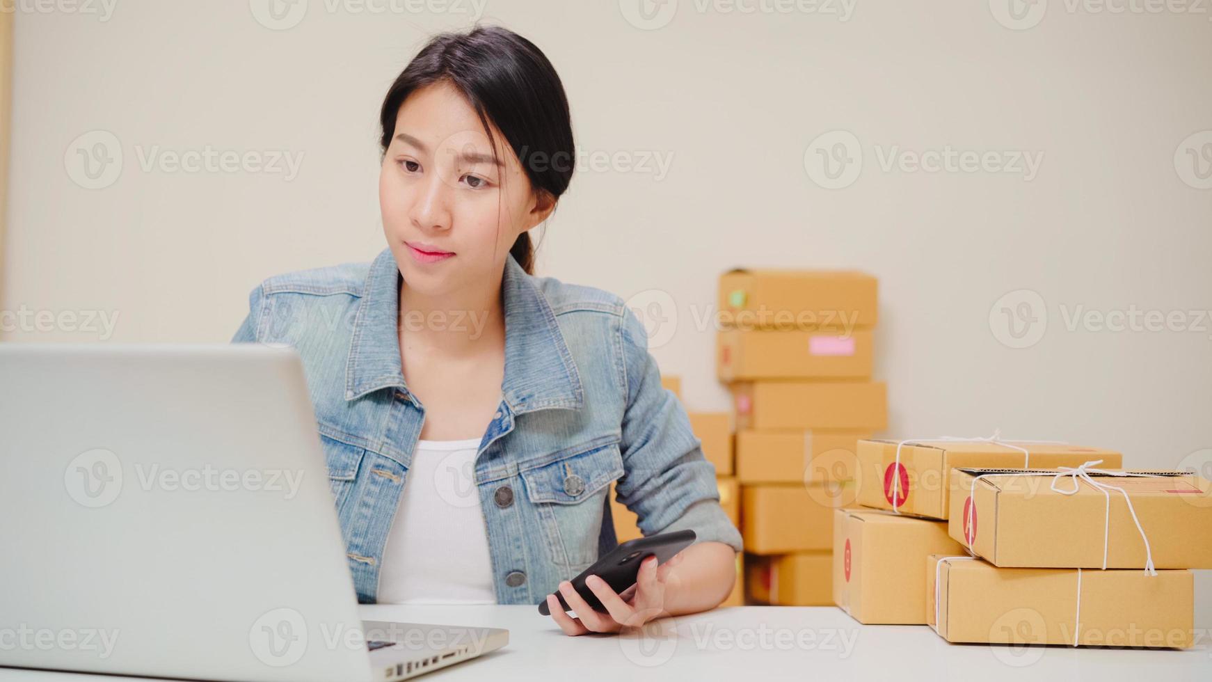 inteligente joven emprendedora asiática propietaria de una pyme que verifica el producto en línea en stock y lo guarda en una computadora portátil que trabaja en casa. propietario de una pequeña empresa en el concepto de oficina en casa. foto