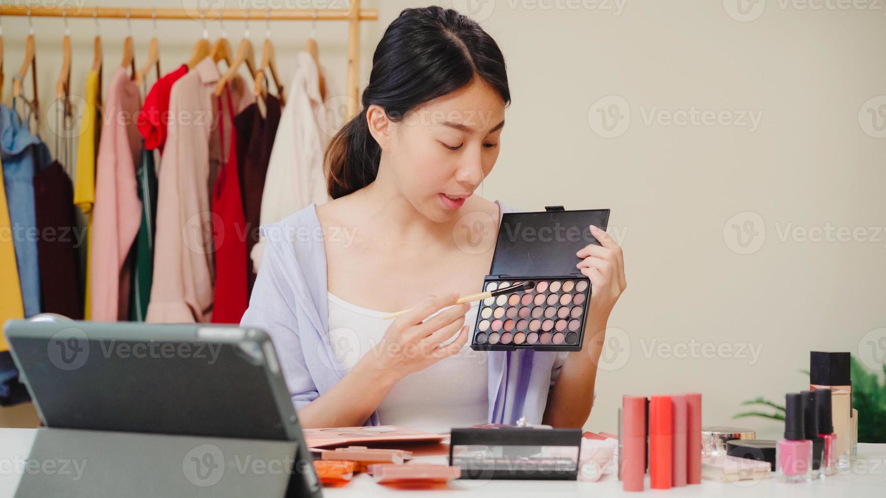 Beauty blogger present beauty cosmetics sitting in front tablet for recording video. Beautiful asian woman use cosmetics review make up tutorial broadcast live video to social network by internet. photo