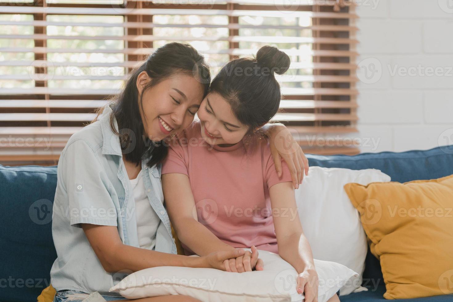 Young Lesbian lgbtq Asian women couple hug and kiss at home. Attractive Asian lover pride female happy relax spend romantic time together while lying sofa in living room concept. photo