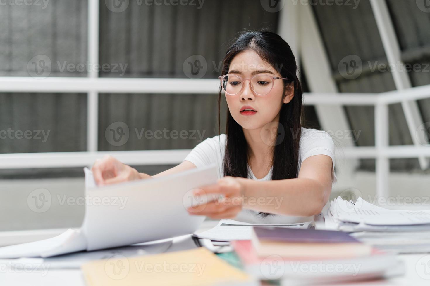 Asian student women reading books in library at university. Young undergraduate girl do homework, read textbook, study hard for knowledge and education on lecture desk at college campus. photo