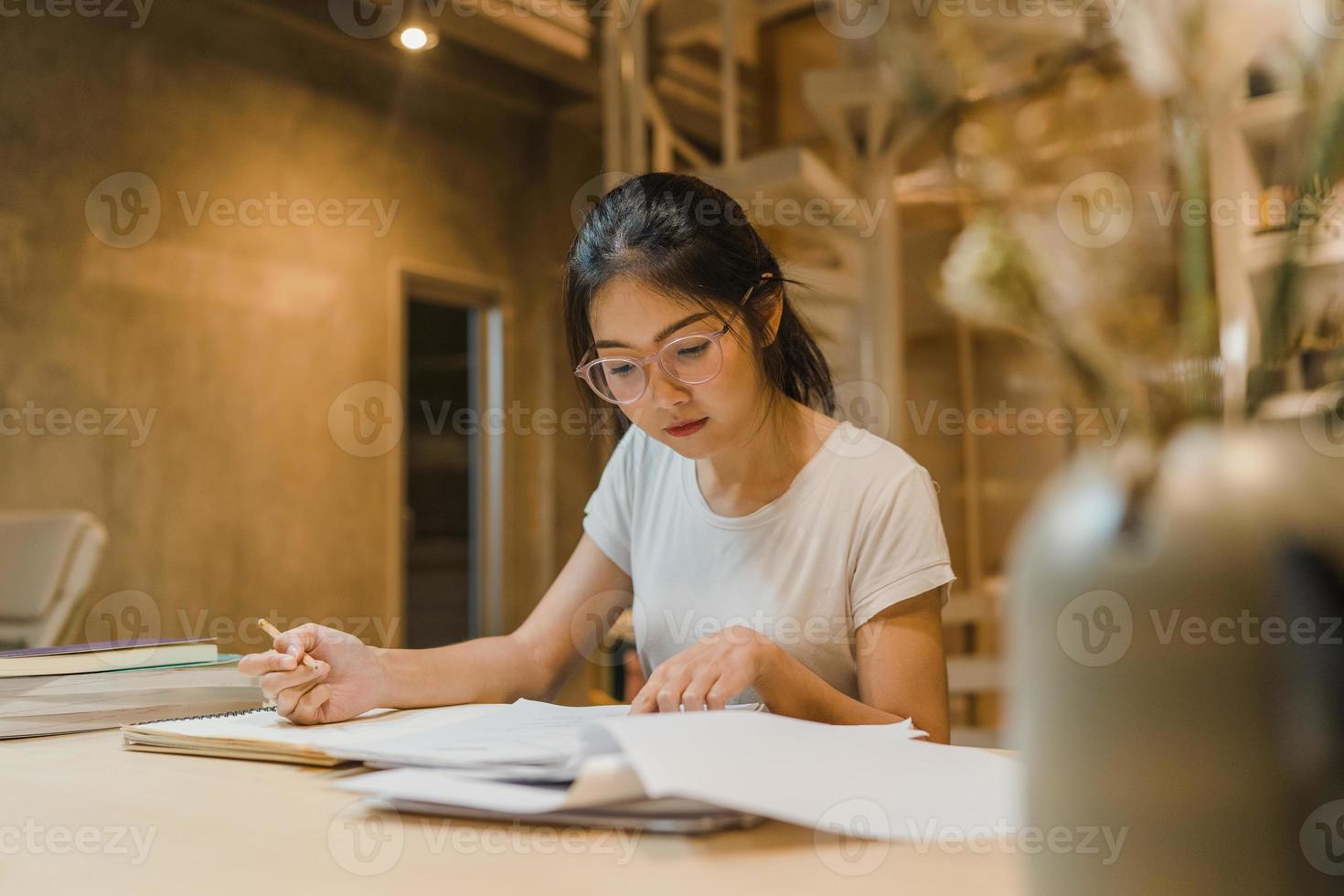 Asian student women reading books in library at university. Young undergraduate girl do homework, read textbook, study hard for knowledge on lecture desk at college campus overtime night. photo