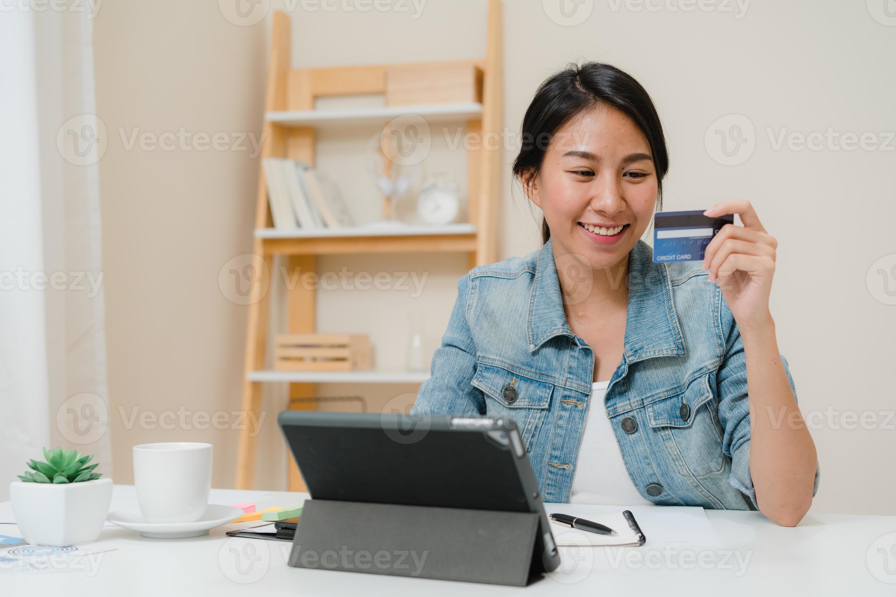hermosa mujer asiática de negocios inteligente que usa una tableta para comprar compras en línea con tarjeta de crédito mientras usa una elegante ropa informal sentada en el escritorio en la sala de estar en casa. mujer de estilo de vida que trabaja en el concepto de hogar. foto