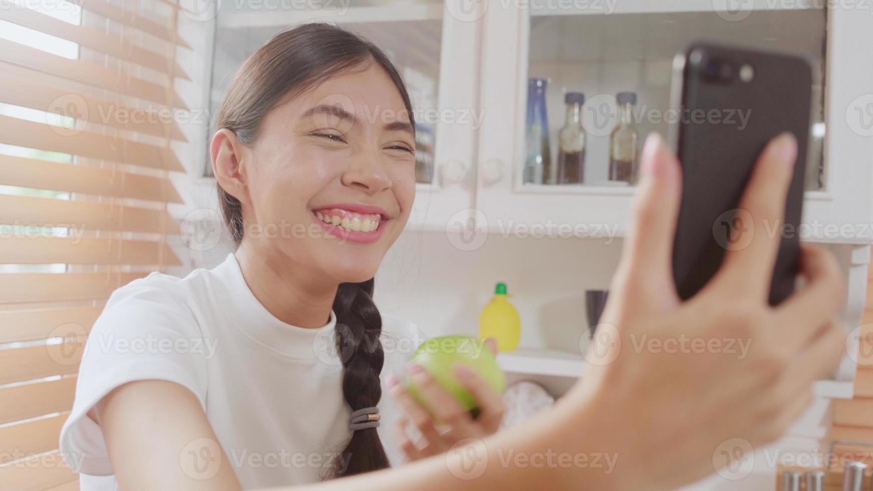 joven mujer adolescente asiática vlog en casa, mujer usando un teléfono inteligente haciendo video vlog en las redes sociales en la cocina. la mujer de estilo de vida se relaja por la mañana en el concepto de casa. foto