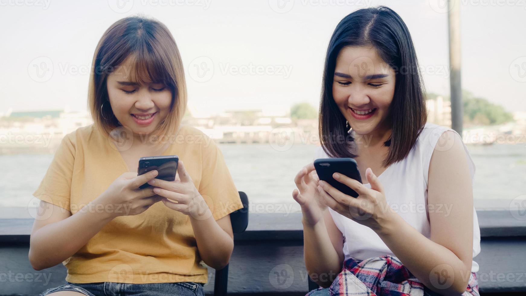 Las jóvenes asiáticas, amigas cercanas, turistas con disfrute informal con un teléfono inteligente comparten una foto en las redes sociales en línea frente al río del puerto de vista en el café de la ciudad, concepto de vacaciones de viaje turístico de estilo de vida.