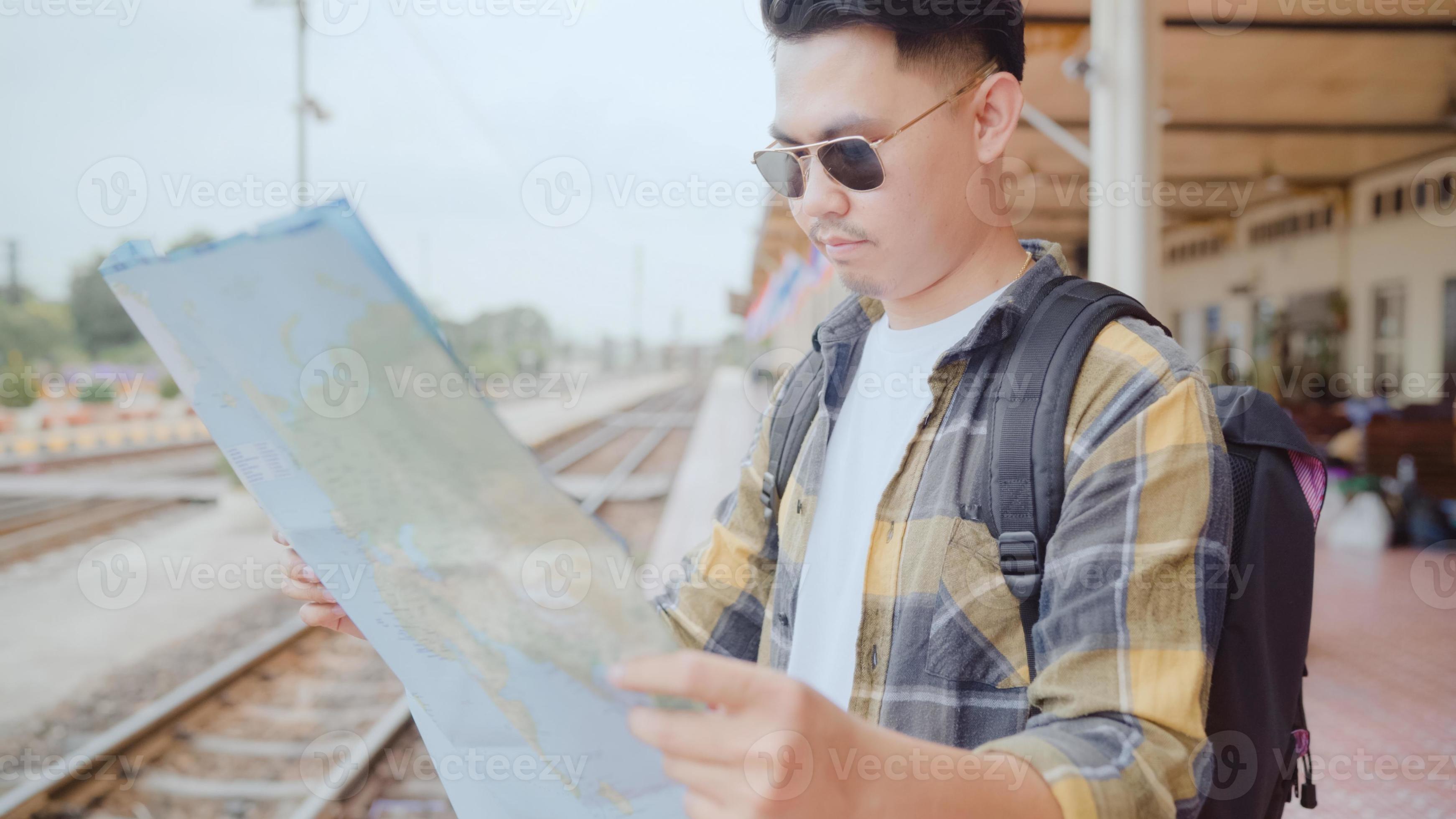 la dirección del hombre asiático del viajero y mirando el mapa de ubicación mientras pasa un viaje de vacaciones y espera el tren en la estación de tren, el joven mochilero turista masculino disfruta del viaje. concepto de viaje de hombres de estilo de vida. foto