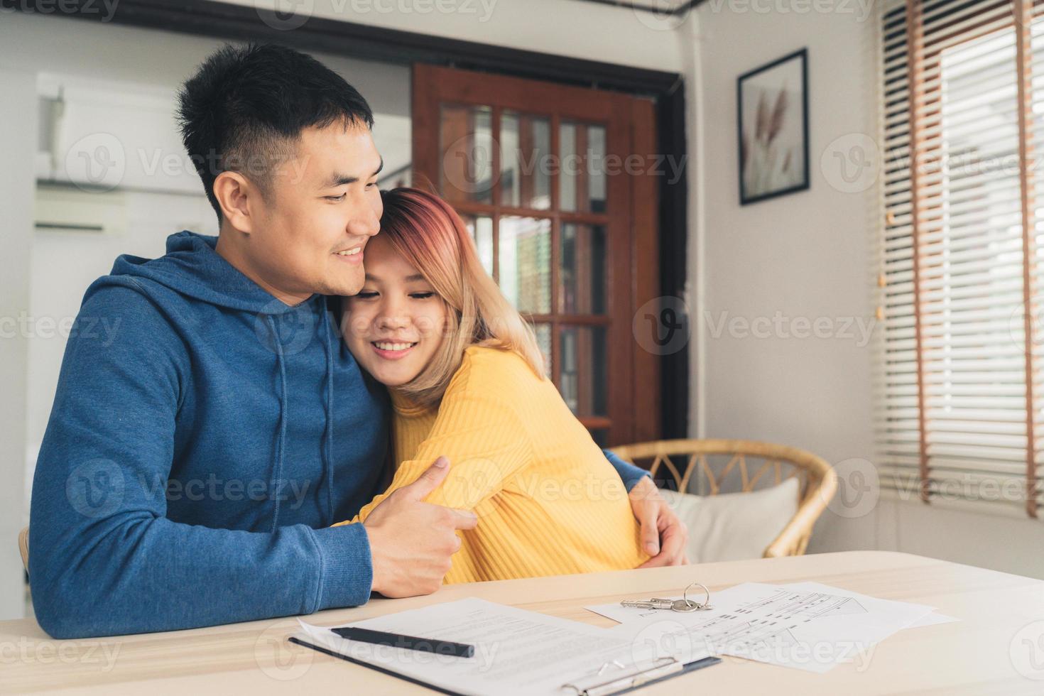 Happy young Asian couple and realtor agent. Cheerful young man signing some documents while sitting at desk together with his wife. Buying new house real estate. Signing good condition contract. photo