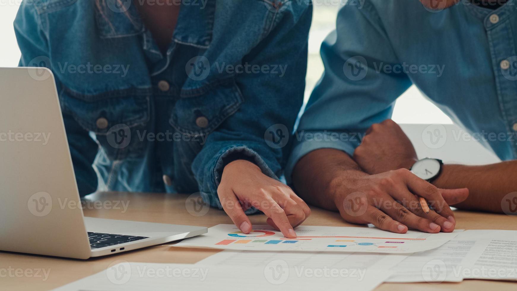 reunión del equipo creativo asiático joven que trabaja en la computadora portátil. grupo de hombres y mujeres de negocios que buscan papel de documento, discuten y piensan en nuevas ideas, situación de negocios, trabajo en equipo en el concepto de oficina moderna. foto