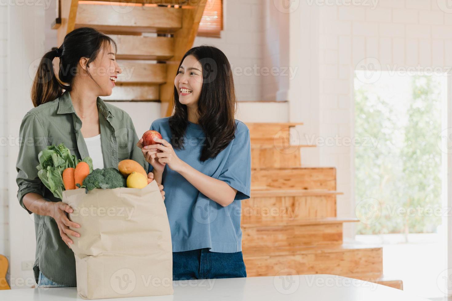 una pareja de mujeres lesbianas lgbtq asiáticas sostienen bolsas de papel de compras en casa, una joven asiática feliz compra verduras y productos saludables de frutas del supermercado y lo pone en la cocina por el concepto de la mañana. foto
