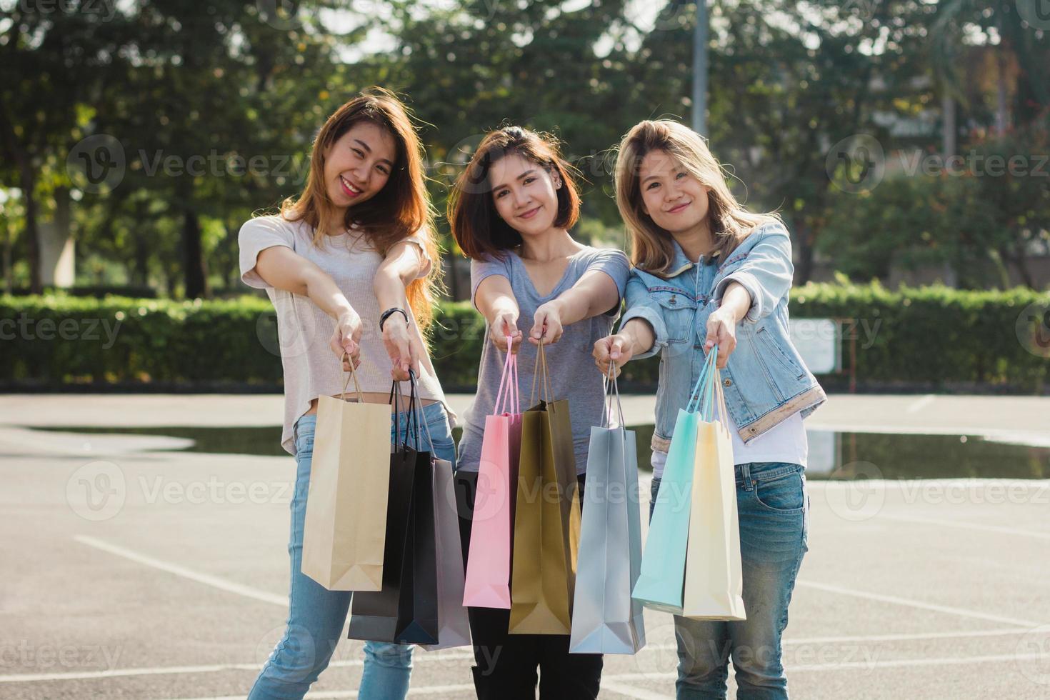 grupo de jóvenes asiáticas comprando en un mercado al aire libre con bolsas de compras en las manos. las jóvenes asiáticas muestran lo que obtuvieron en una bolsa de compras bajo la cálida luz del sol. concepto de compras al aire libre en grupo. foto