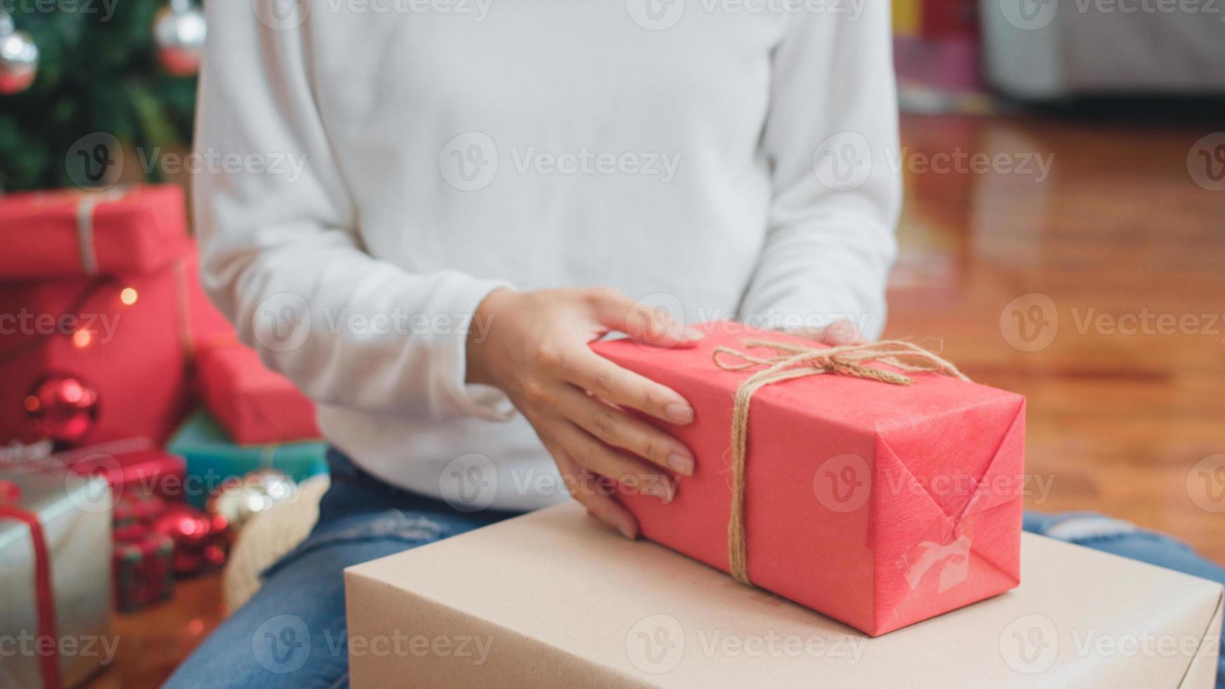 Asian women celebrate Christmas festival. Female teen wear sweater and Christmas hat relax happy wrapping gifts near Christmas tree enjoy xmas winter holidays together in living room at home. photo