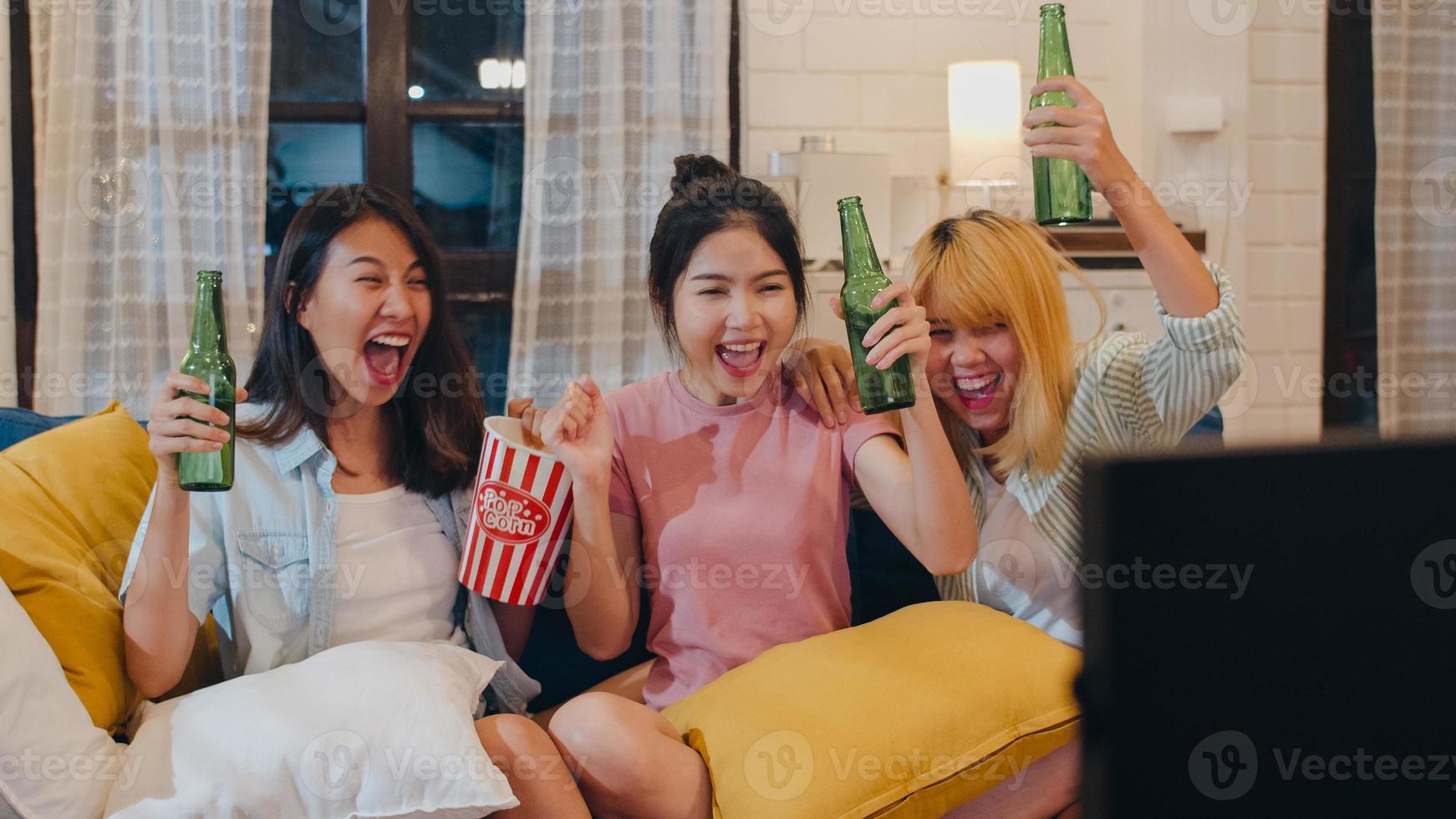 Group of Asian women party at home, female drinking beer watching TV cheer soccer funny moment together on sofa in living room in night. Teenager young friend football fan, celebrate holiday concept. photo
