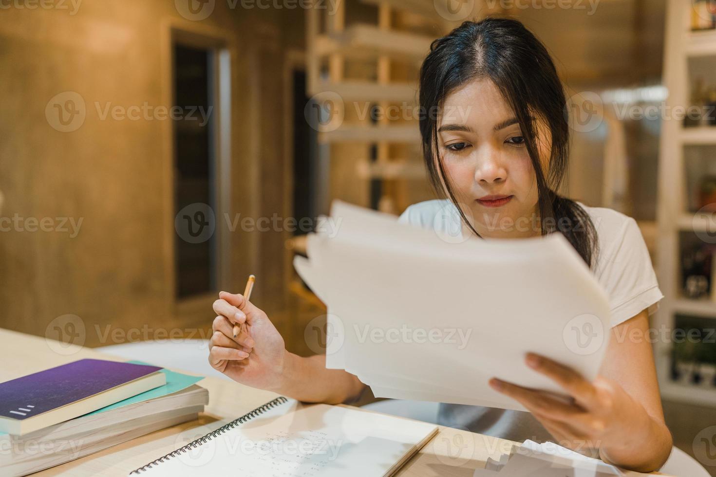 Asian student women reading books in library at university. Young undergraduate girl do homework, read textbook, study hard for knowledge on lecture desk at college campus overtime night. photo