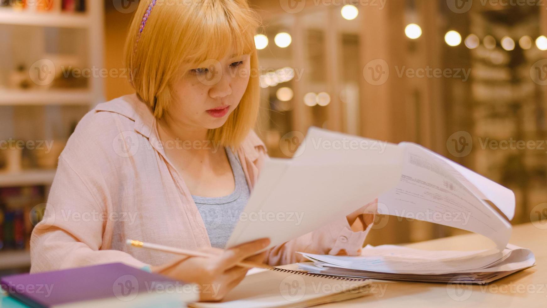 Asian student women reading books in library at university. Young undergraduate girl do homework, read textbook, study hard for knowledge on lecture desk at college campus overtime night. photo