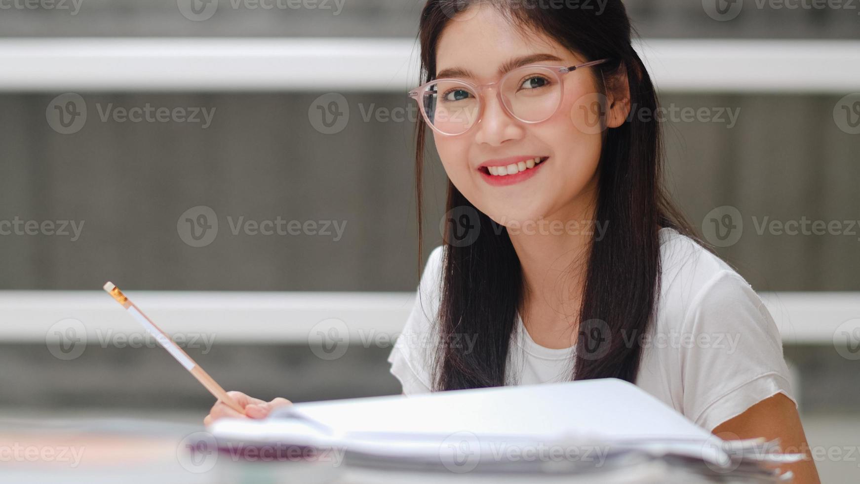 Asian student women reading books in library at university. Young undergraduate girl do homework, read textbook, study hard for knowledge and education on lecture desk at college campus. photo