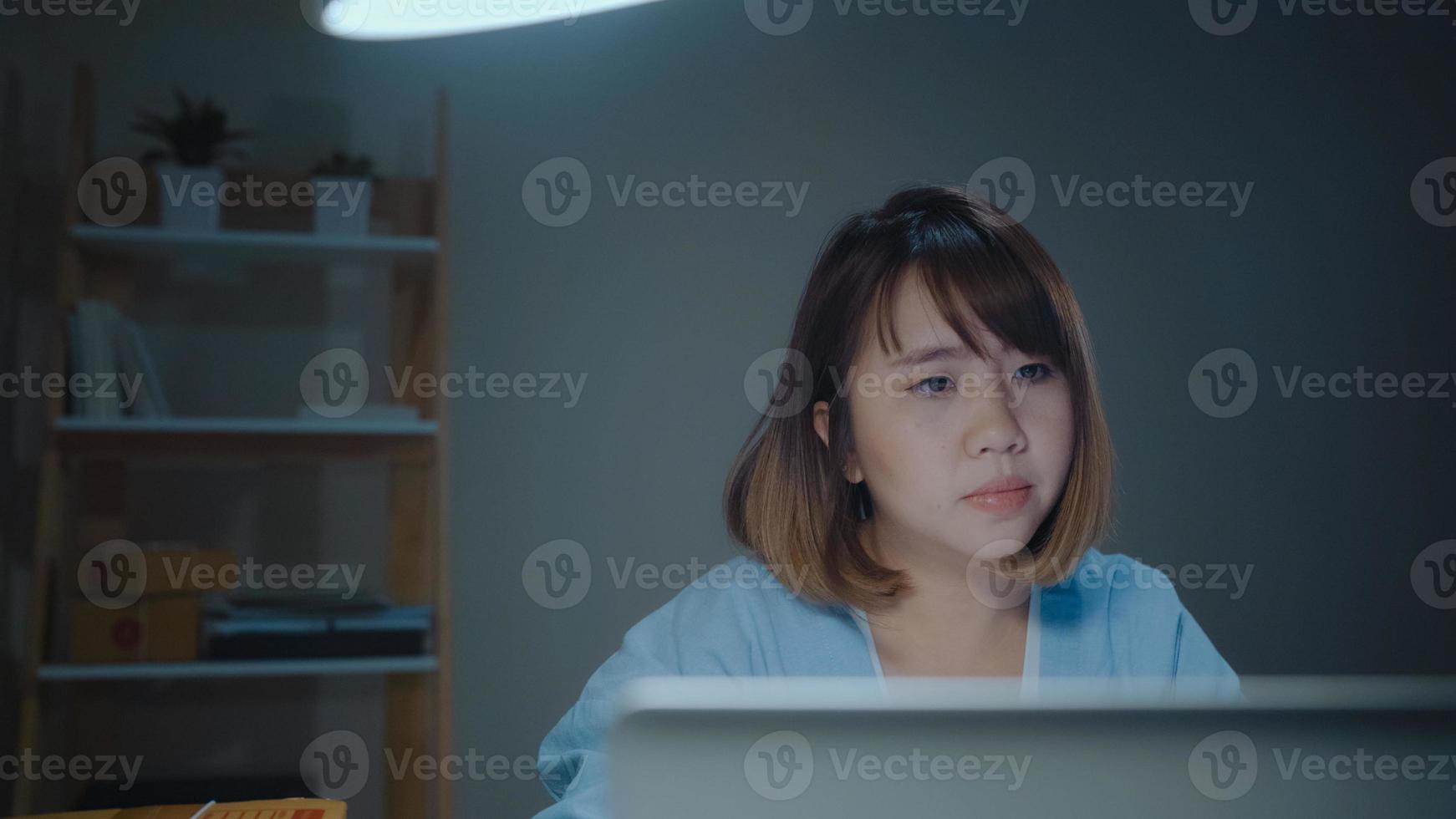 Young Asian entrepreneur business woman owner of SME online checking product on stock and save to laptop working in night at home. Feeling sick and tired. Small business owner at home office concept. photo