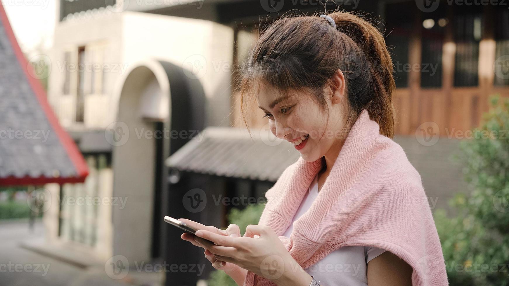 Cheerful Asian backpacker blogger woman using smartphone for direction and looking on location map while traveling at Chinatown in Beijing, China. Lifestyle backpack tourist travel holiday concept. photo