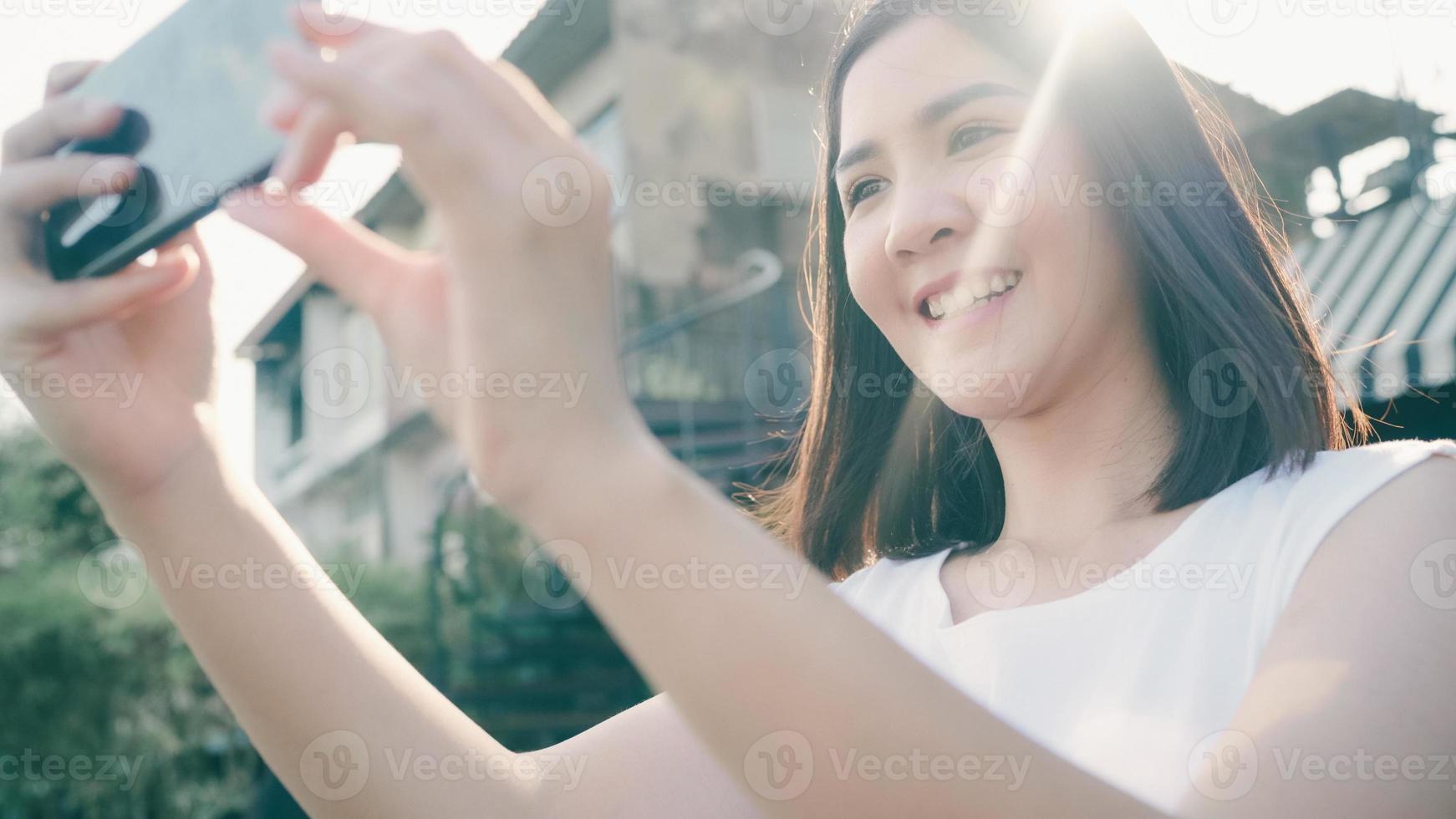 Young Asian woman blogger tourist use smartphone take photo in front of port river feel happy joyful with beautiful sun light travel at cafe city town , Lifestyle tourist travel holiday concept.