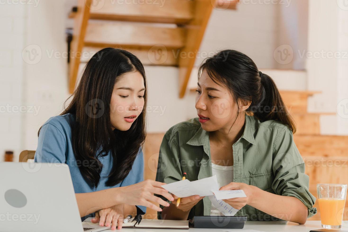 Business Asian Lesbian lgbtq women couple do account at home, Young Asia girl serious, stress while using calculator record budget, tax, financial document on laptop working in kitchen concept. photo