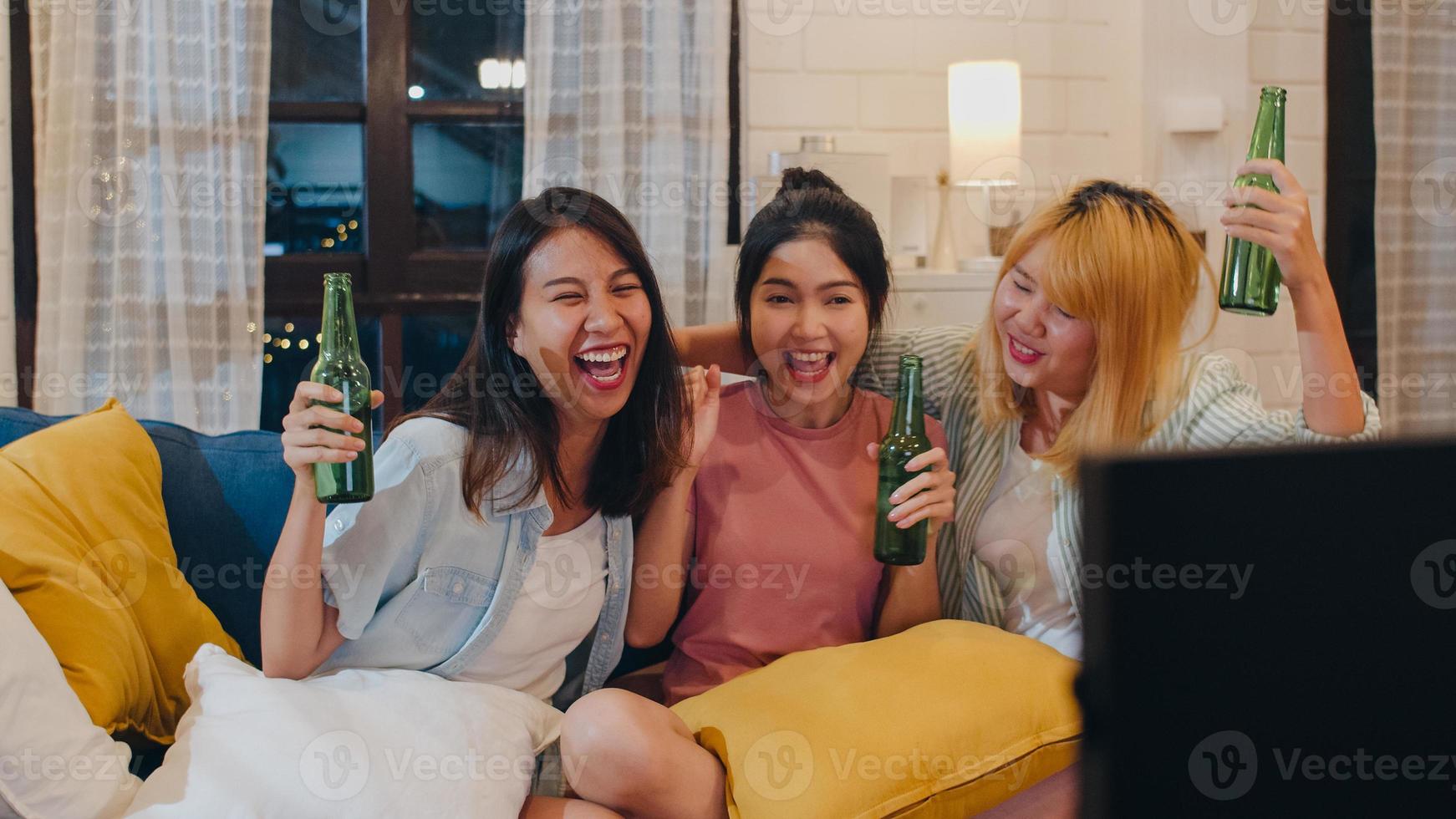 Group of Asian women party at home, female drinking beer watching TV cheer soccer funny moment together on sofa in living room in night. Teenager young friend football fan, celebrate holiday concept. photo