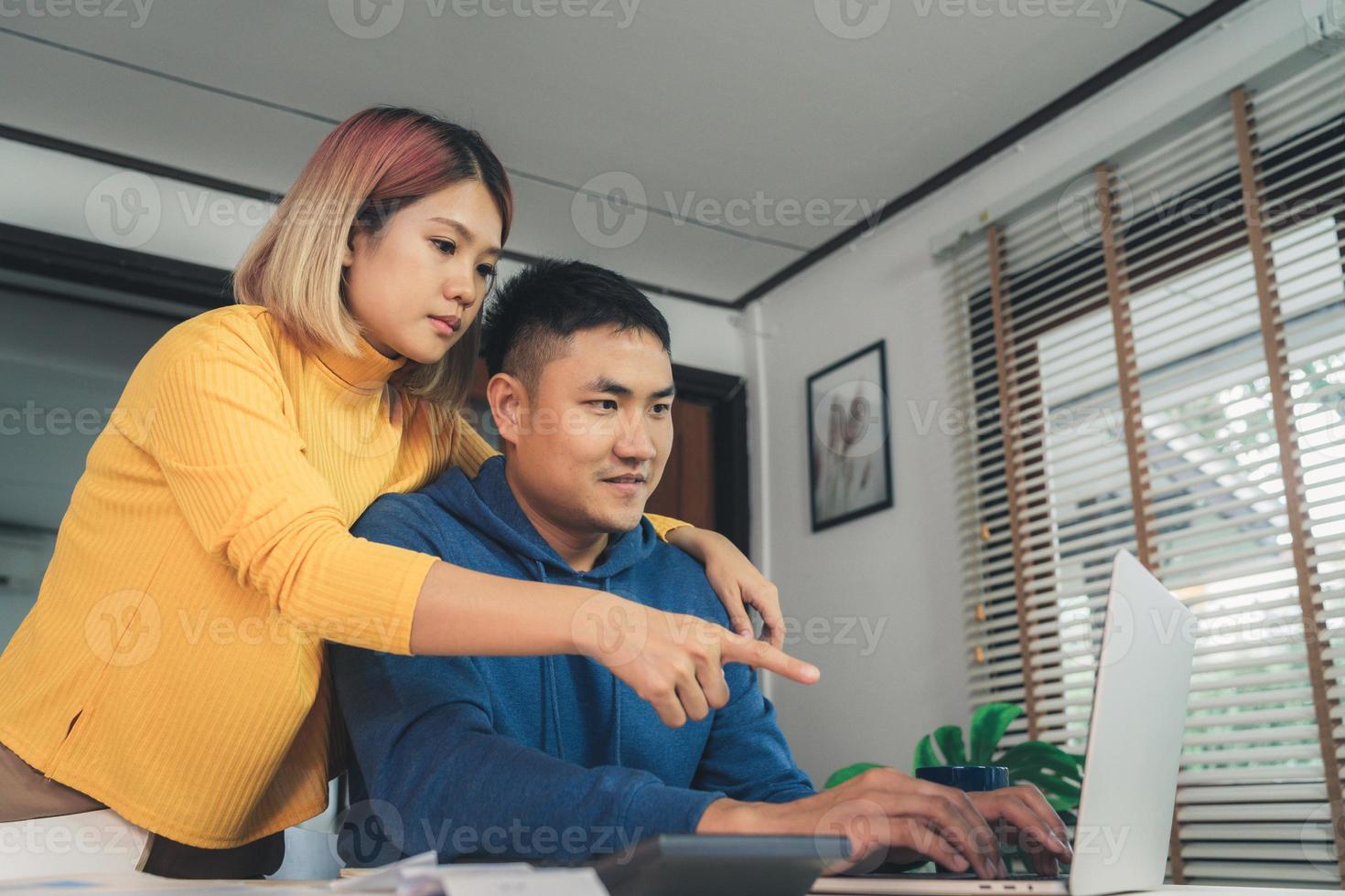 Young asian couple managing finances, reviewing their bank accounts using laptop computer and calculator at modern home. Woman and man doing paperwork together, paying taxes online on notebook pc. photo