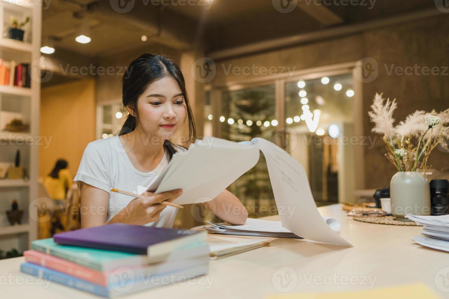 Asian student women reading books in library at university. Young undergraduate girl do homework, read textbook, study hard for knowledge on lecture desk at college campus overtime night. photo