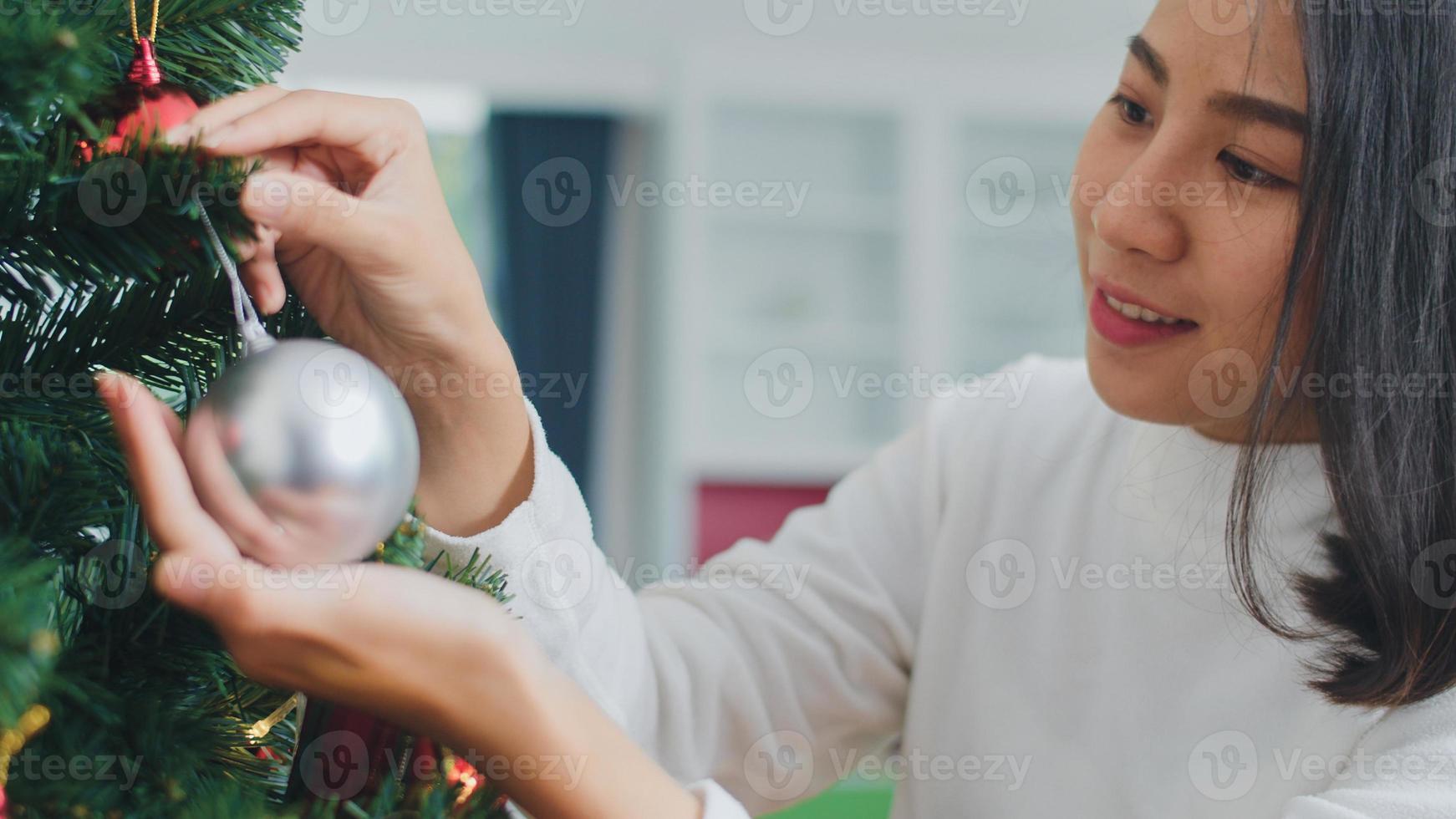 las mujeres asiáticas decoran el árbol de navidad en el festival de navidad. adolescente feliz sonriendo celebra las vacaciones de invierno de Navidad en la sala de estar en casa. fotografía de cerca. foto