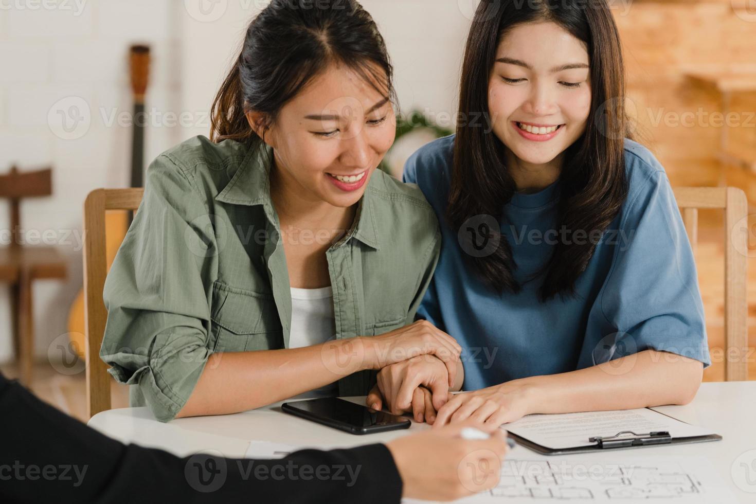 Asian Lesbian lgbtq women couple sign contract at home, Young couple consulting with real estate financial advisor, Buying new house and handshaking with broker in living room concept. photo