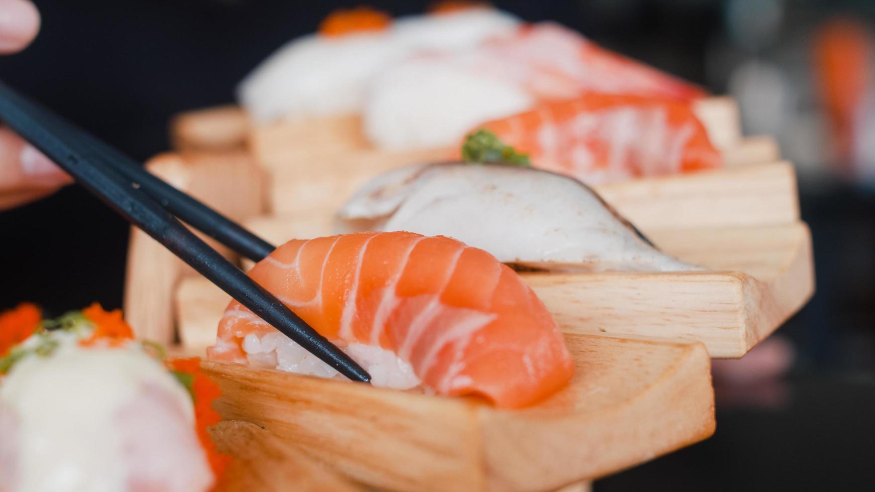 Asian woman eating sushi in japanese restaurant, young female holding chopsticks and eating salmon sushi in lunch time in summer. Lifestyle women eating traditional food concept. photo