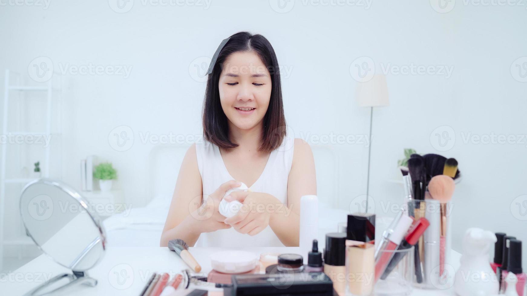 Beauty blogger present beauty cosmetics sitting in front camera for recording video. Happy beautiful young Asian woman use cosmetics review make up tutorial broadcast live video to social network. photo