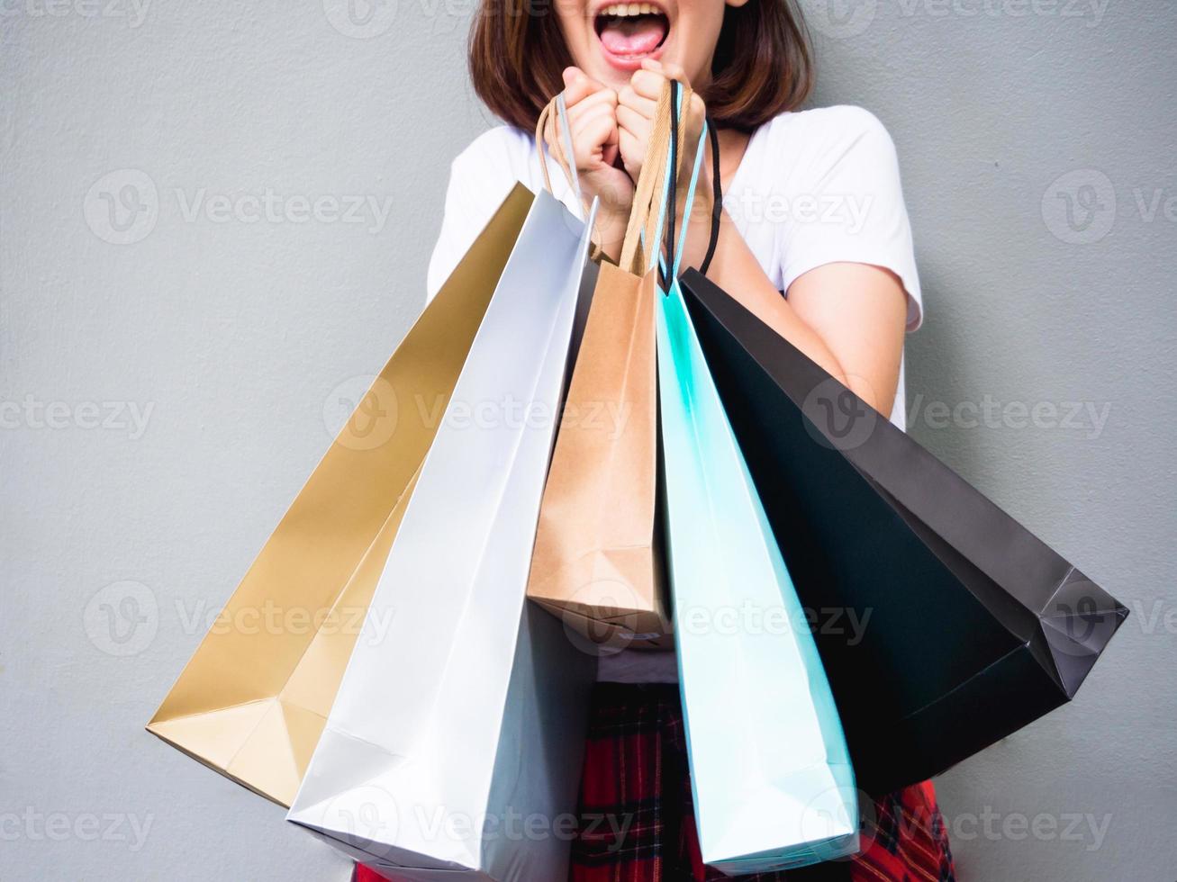 Young happy summer shopping asian woman with shopping bags on grey background at copy space. Beautiful young mixed race asian woman. Chinese asian woman shopper smiling happy. photo