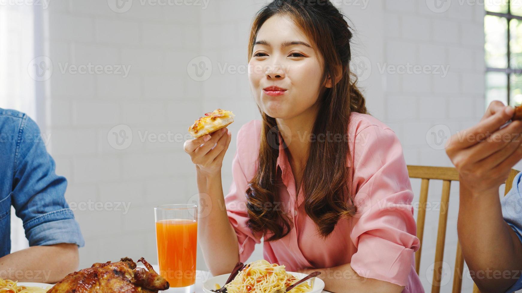 feliz grupo de jóvenes amigos almorzando en casa. fiesta familiar de asia comiendo pizza y riéndose disfrutando de la comida mientras se sientan juntos en la mesa de comedor en casa. celebración de vacaciones y unión. foto