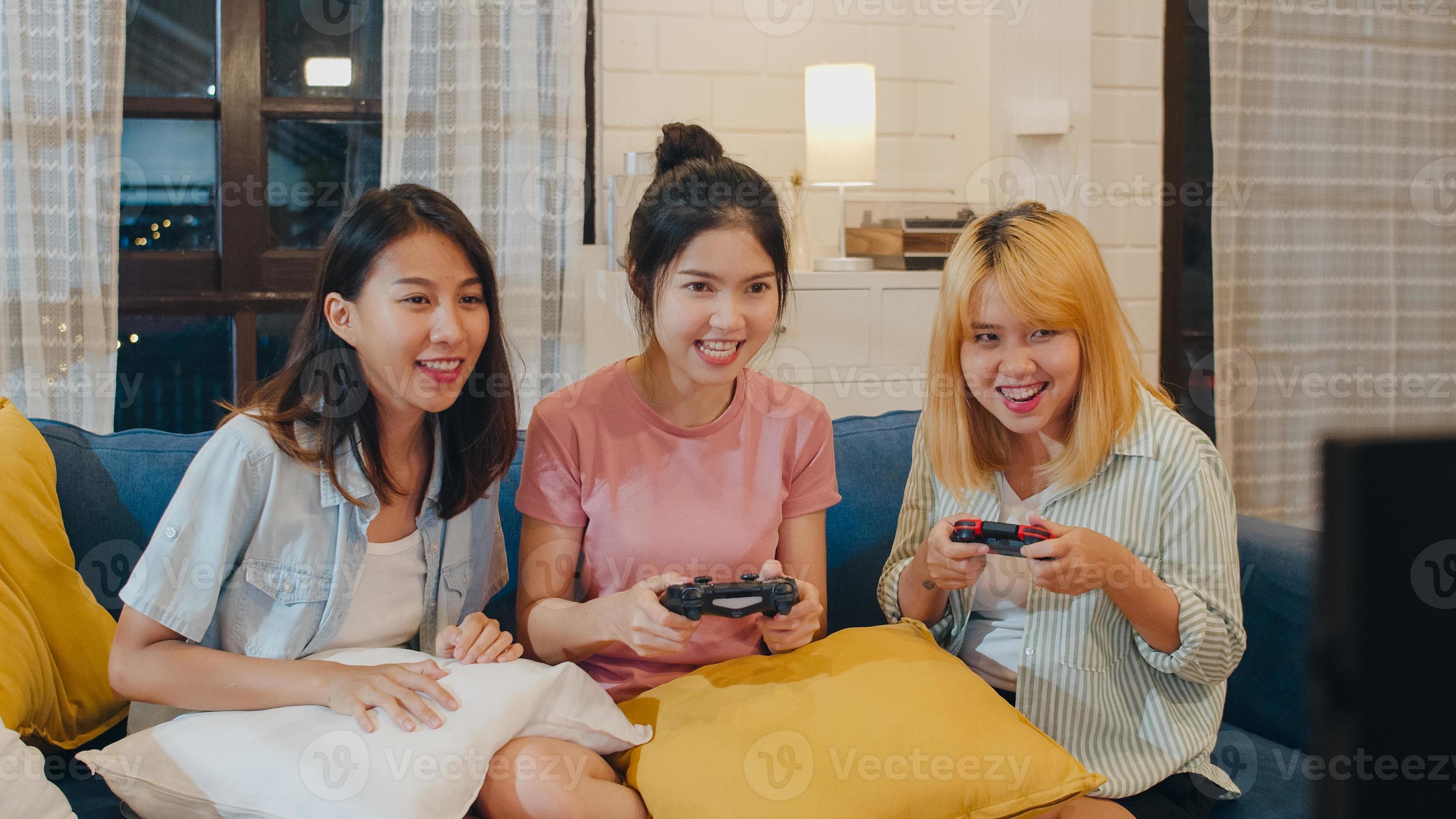 Group of Asian women couple play games at home, female using joystick  having funny moment together on sofa in living room in night. Teenager  young friend football fan, celebrate holiday concept. 5492927