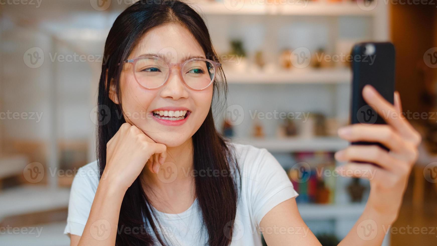 Blogger Asian friendly women influencer waving hand making video call at night cafe. Young lady happy relax fun using technology mobile phone record vlog upload in social media at college campus. photo