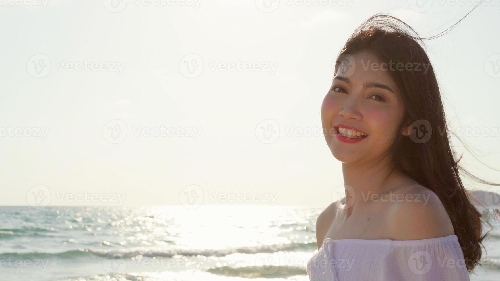 joven mujer asiática que se siente feliz en la playa, hermosa mujer feliz relajarse sonriendo diversión en la playa cerca del mar cuando se pone el sol por la noche. las mujeres de estilo de vida viajan en concepto de playa. foto