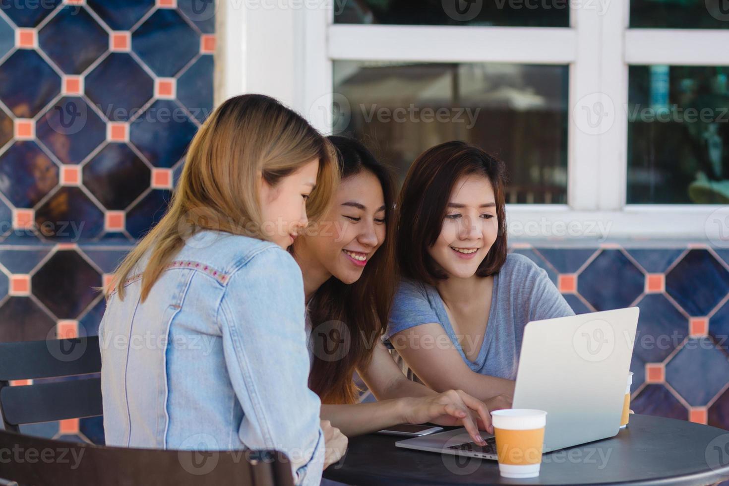 Group of beautiful smart business freelance Asian women in smart casual wear working together on laptop or computer while sitting on table in creative office or cafe. photo