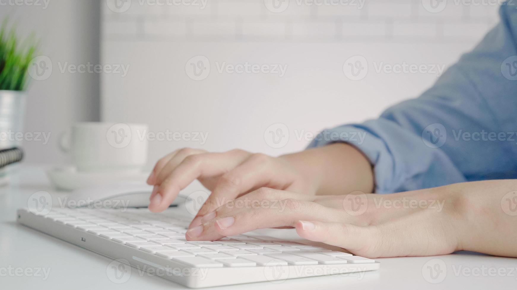 Beautiful young smiling Asian woman working on laptop while at home in office work space. Businesswoman working from home via portable computer writing on keyboard. Enjoying time at home. photo