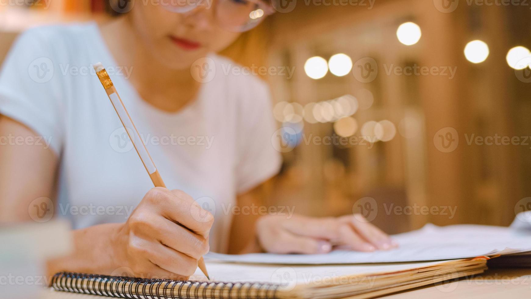 Asian student women reading books in library at university. Young undergraduate girl do homework, read textbook, study hard for knowledge on lecture desk at college campus overtime night. photo