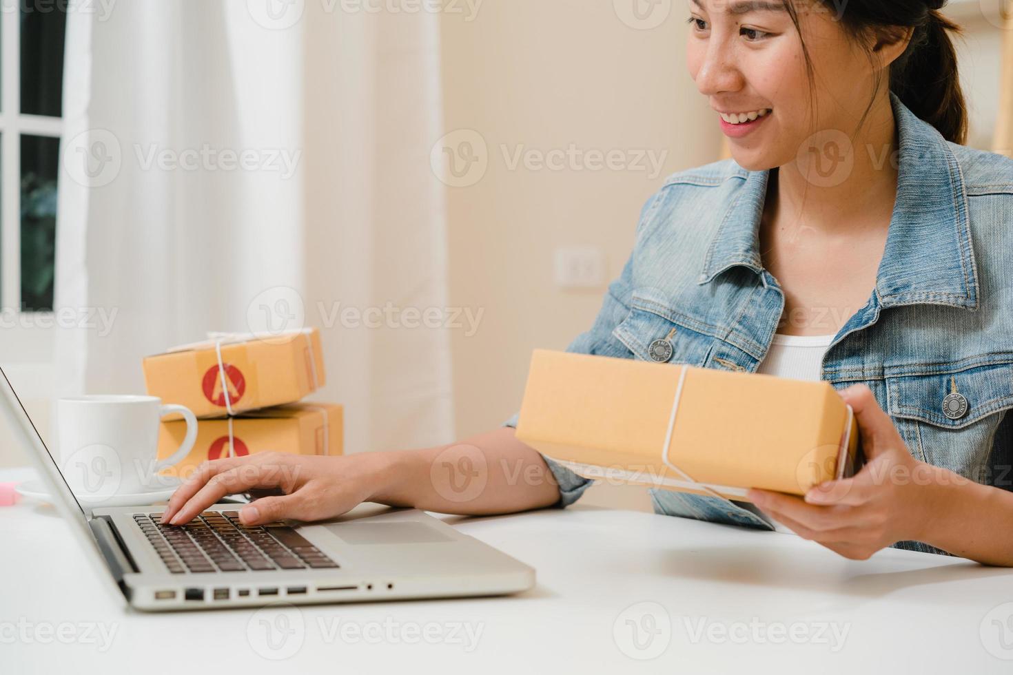 Beautiful smart Asian young entrepreneur business woman owner of SME online checking product on stock and save to computer working at home. Small business owner at home office concept. photo
