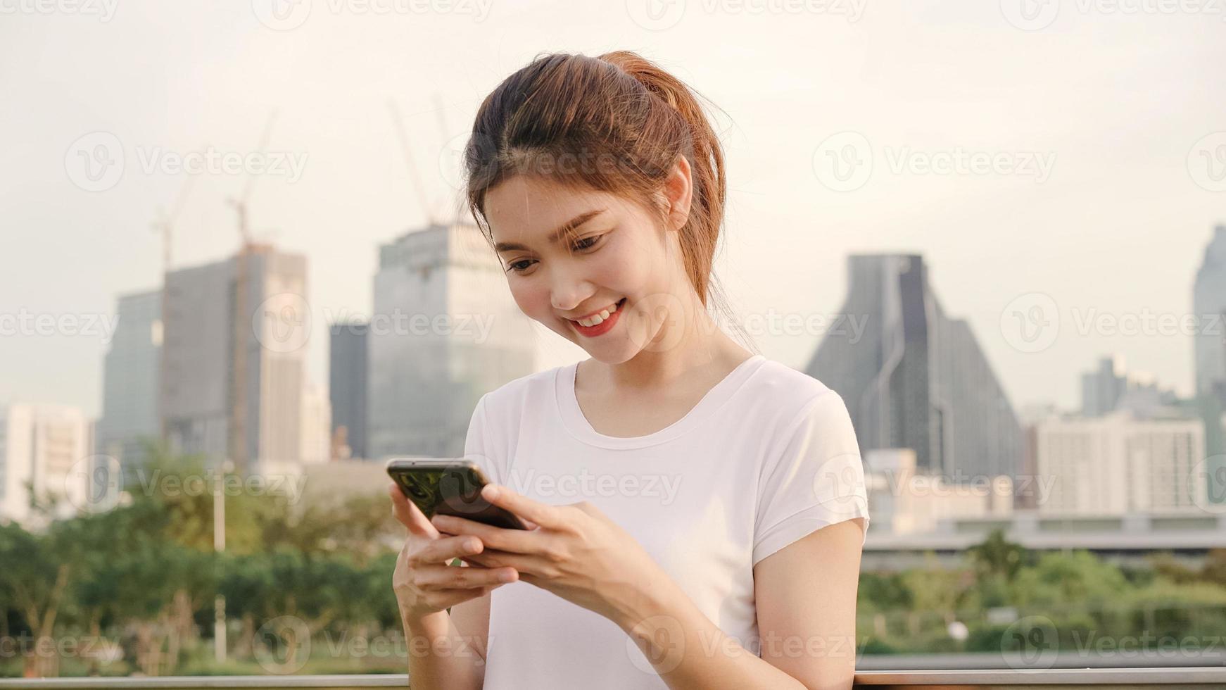 Cheerful Asian tourist blogger woman using smartphone for direction and looking on location map while traveling on the street at downtown city. Lifestyle backpack tourist travel holiday concept. photo