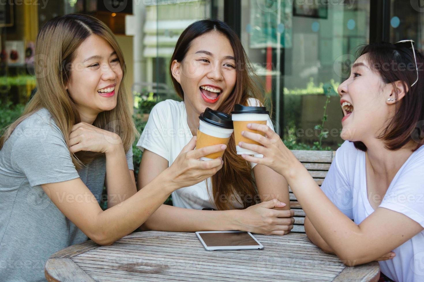 alegres jóvenes asiáticas sentadas en un café tomando café con amigos y hablando juntas. atractiva mujer asiática disfrutando del café. chicas divirtiéndose en casa y riendo. foto