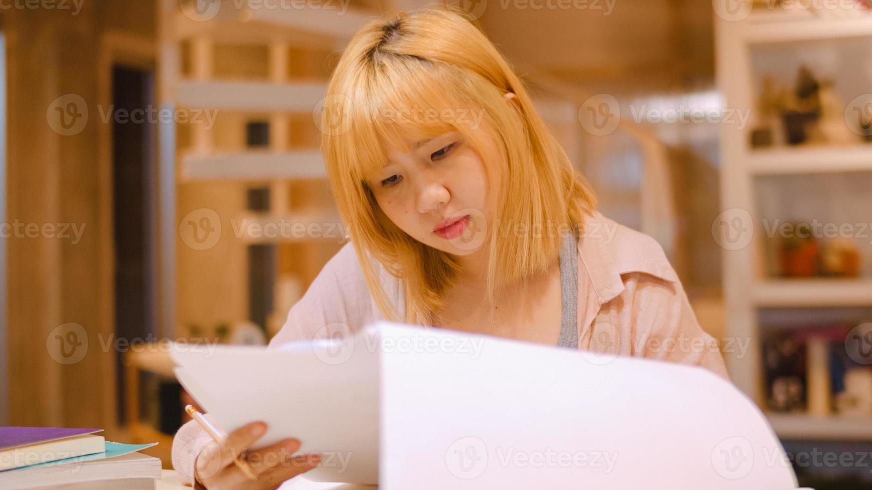 Asian student women reading books in library at university. Young undergraduate girl do homework, read textbook, study hard for knowledge on lecture desk at college campus overtime night. photo
