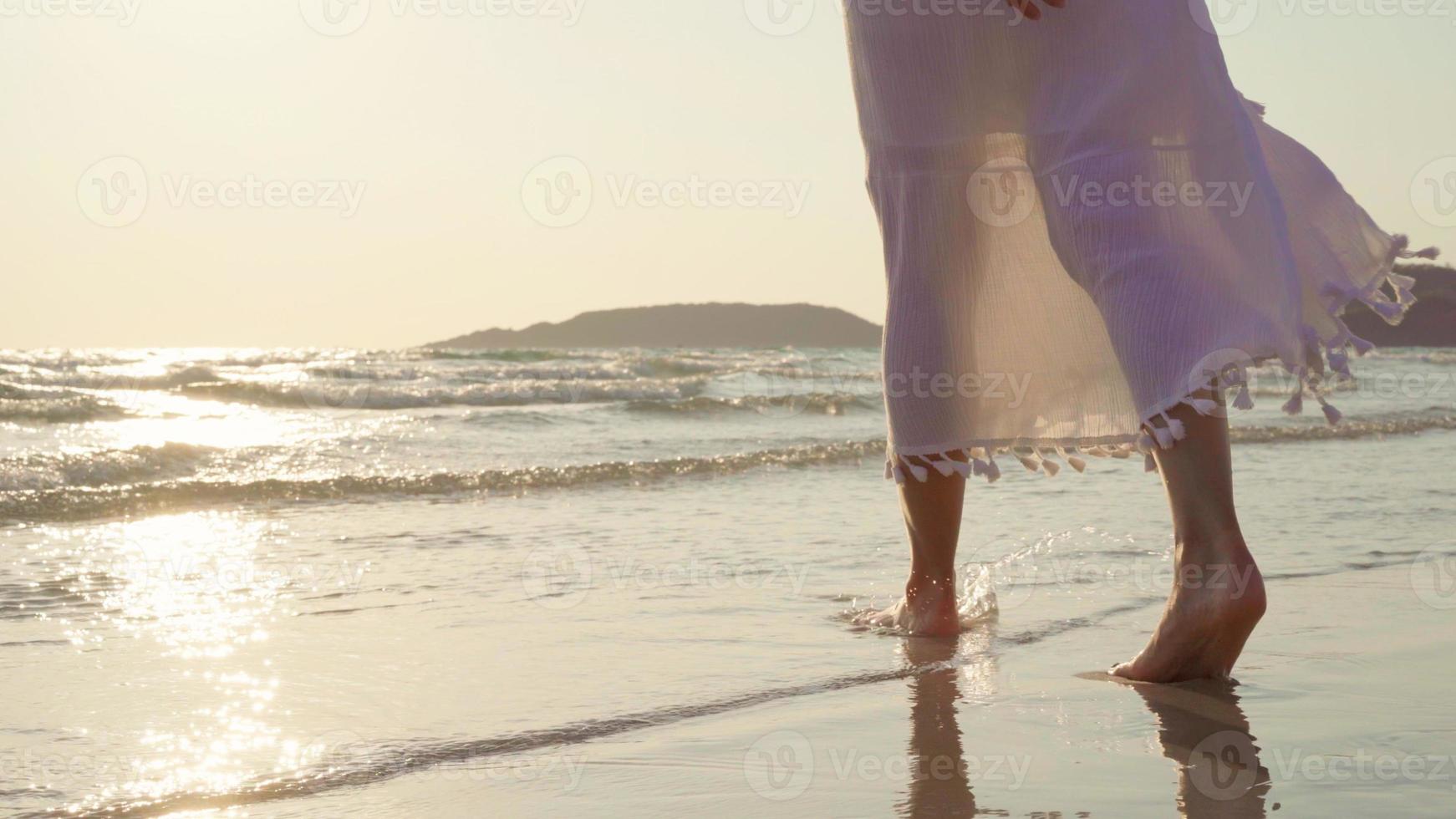 joven mujer asiática caminando en la playa. hermosa mujer feliz relajarse caminando en la playa cerca del mar al atardecer en la noche. las mujeres de estilo de vida viajan en concepto de playa. foto