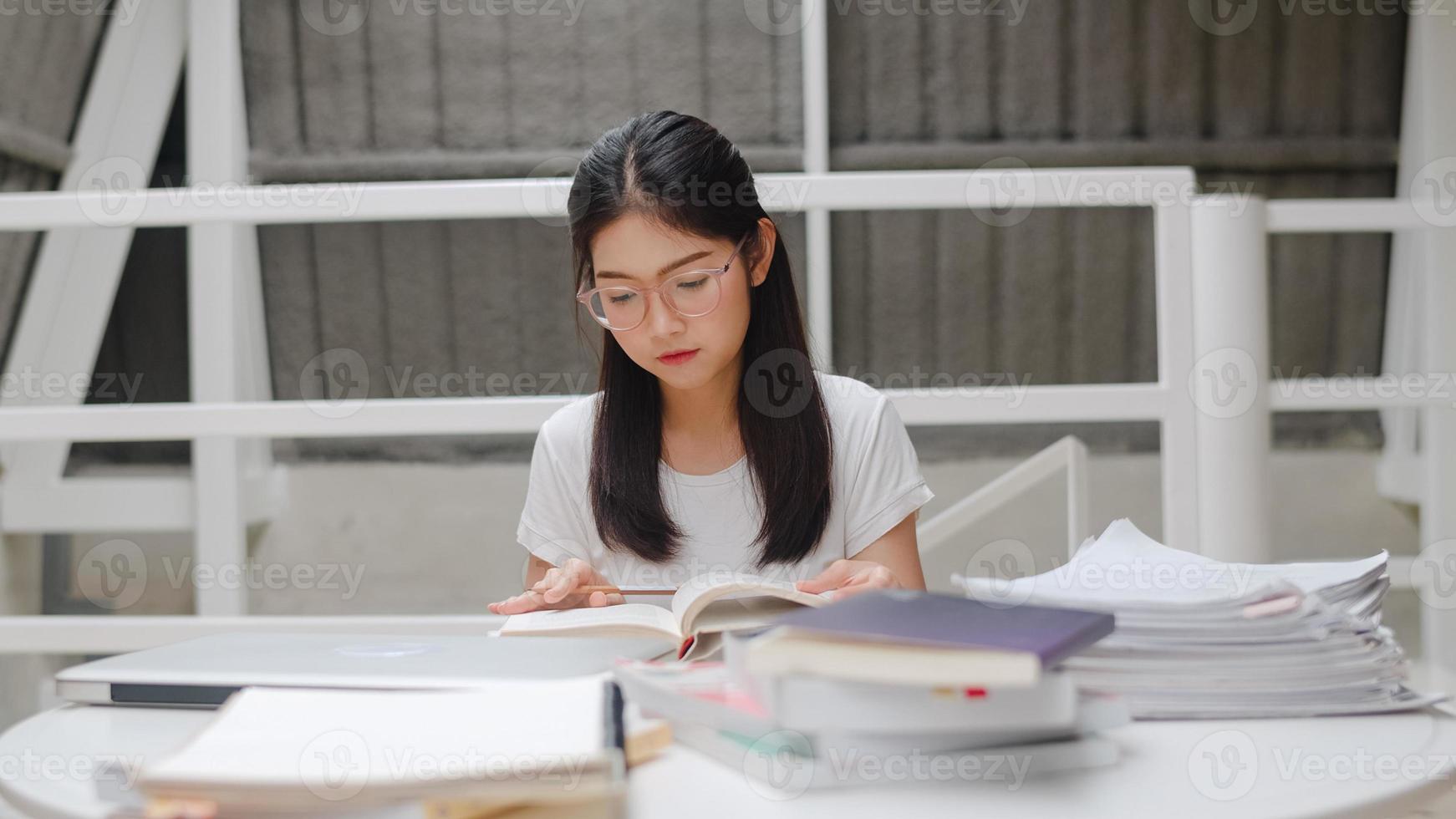 mujeres estudiantes asiáticas leyendo libros en la biblioteca de la universidad. la joven estudiante hace la tarea, lee libros de texto, estudia mucho para obtener conocimiento y educación en el escritorio de conferencias en el campus universitario. foto
