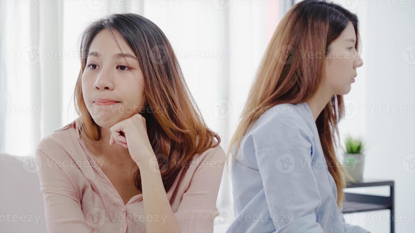 Unhappy Asian lesbian lgbt couple sitting each side of sofa with moody emotion in living room. Women conflict with her girlfriend and have bad relationship at home. photo